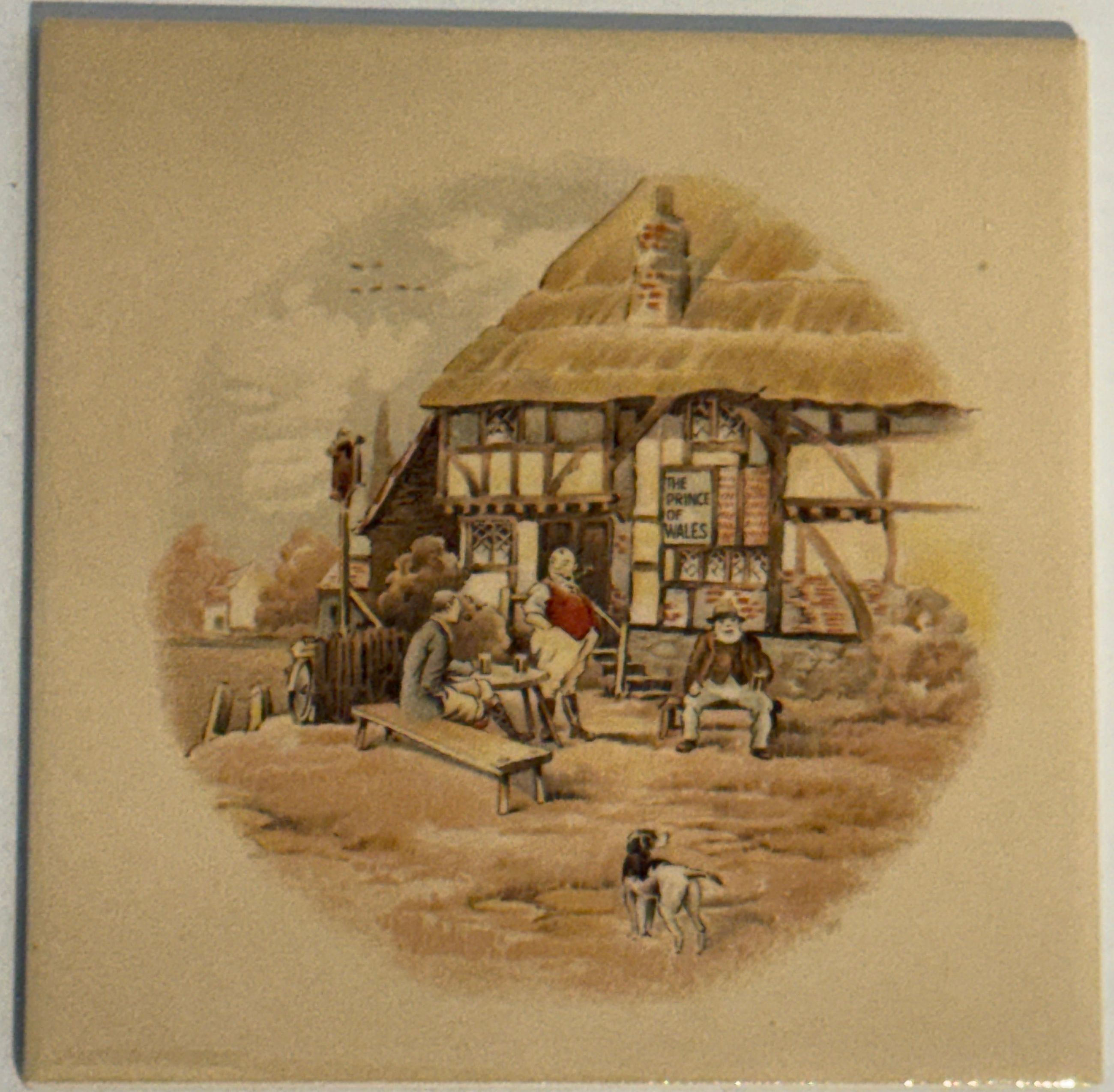 Historische englische Motivfliese: Fachwerk-Wirtshaus mit Strohdach und Schild "The Prince of Wales", davor Männer beim Trinken und ein schwarz-weißer Hund